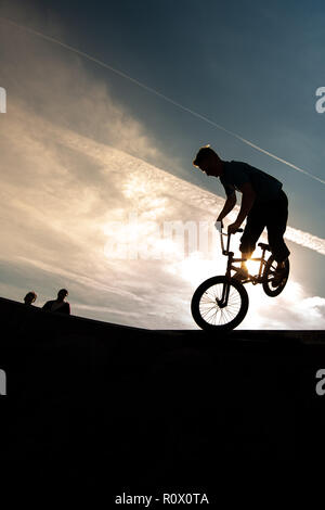 Un rider de bmx au Plaza, Central Forest Park à Stoke on Trent haut perchés et tombé sur une bande en silhouette au coucher du soleil Banque D'Images