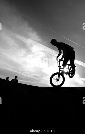 Un rider de bmx au Plaza, Central Forest Park à Stoke on Trent haut perchés et tombé sur une bande en silhouette au coucher du soleil Banque D'Images