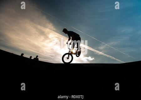 Un rider de bmx au Plaza, Central Forest Park à Stoke on Trent haut perchés et tombé sur une bande en silhouette au coucher du soleil Banque D'Images