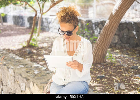 Belle femme d'âge moyen qui travaille à l'extérieur dans le parc avec une tablette moderne à l'aide d'internet et d'un périphérique d'affichage de l'écran tactile. Bureau extérieur dans un ordinateur portable Banque D'Images