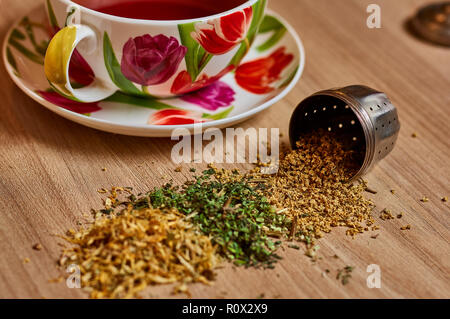 Le thé de répandre de la crépine d'oeufs métal avec tasse de thé en arrière-plan Banque D'Images