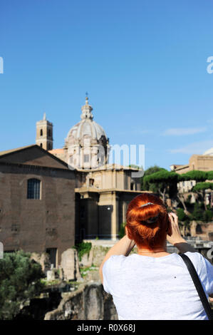 Jeune femme cheveux rouge prendre photo avec smartphone à des Forums Impériaux (Fori Imperiali) à Rome. Banque D'Images