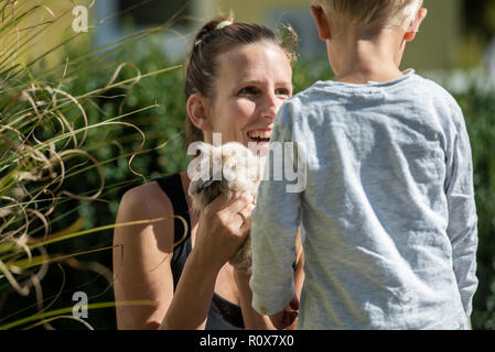 Happy young mother holding baby rabbit fourrure le montrer à l'extérieur de son petit garçon sur une journée ensoleillée. Banque D'Images