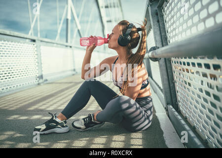 Jeune femme est remise en forme se reposant après un entraînement intensif sur le pont de la rivière et l'eau potable. Banque D'Images