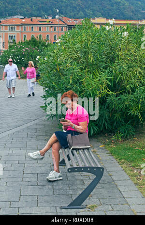 Tourisme mature woman sitting on park bench lecture texte smartphone à Côme, Italie Banque D'Images