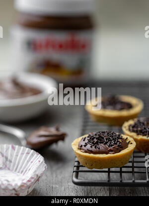 Tartelettes nutella avec des vermicelles de chocolat sur un support avec du Nutella en rack à l'arrière-plan Banque D'Images