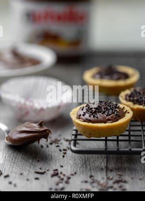 Tartelettes nutella avec des vermicelles de chocolat sur un support avec du Nutella en rack à l'arrière-plan Banque D'Images