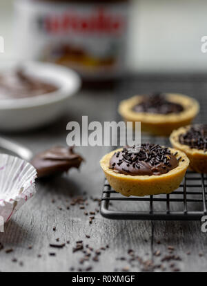 Tartelettes nutella avec des vermicelles de chocolat sur un support avec du Nutella en rack à l'arrière-plan Banque D'Images