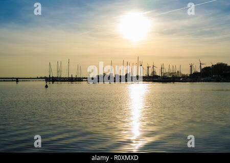 Belle vue sur le coucher de soleil derrière le port en laissant une silhouette d'éoliennes et des bateaux à voile avec leur mât sur l'île de Fehmarn dans... Banque D'Images