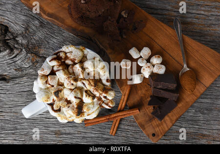 Coup de frais généraux d'une grande tasse de chocolat chaud avec des guimauves grillées à côté d'une planche à découper, morceaux de chocolat cannelle et les cookies. Banque D'Images