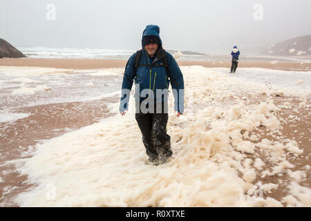 Les randonneurs de spume ou écume de mer d'être soufflé le long de la plage de Sandwood Bay lors de coups de vent, Sutherland, Scotland, UK. Banque D'Images