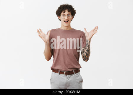 Portrait de surpris beau jeune homme élégant et artistique avec moustache cheveux frisés et bras tatoués gesticulant avec soulevées palms façonnage grand élément étant impressionné et étonné avec la taille Banque D'Images