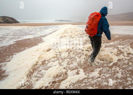 Les randonneurs de spume ou écume de mer d'être soufflé le long de la plage de Sandwood Bay lors de coups de vent, Sutherland, Scotland, UK. Banque D'Images