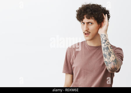 Dis encore une fois ne peut pas entendre clairement. Portrait de beau jeune homme élégant intense avec curly hairstyle moustache et des tatouages bras tenant la main près de demander de répéter la question de l'oreille l'accent gazign at camera Banque D'Images