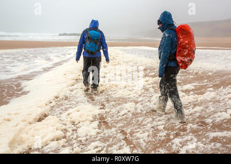 Les randonneurs de spume ou écume de mer d'être soufflé le long de la plage de Sandwood Bay lors de coups de vent, Sutherland, Scotland, UK. Banque D'Images