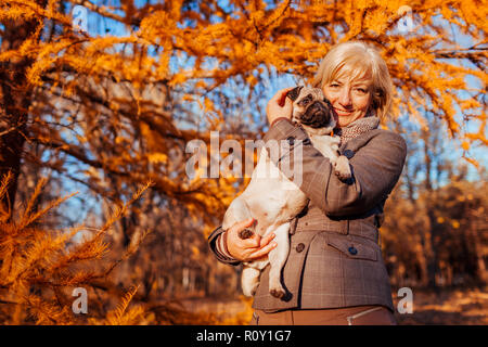 Balades maître chien pug in autumn park. Happy woman hugging pet. Banque D'Images