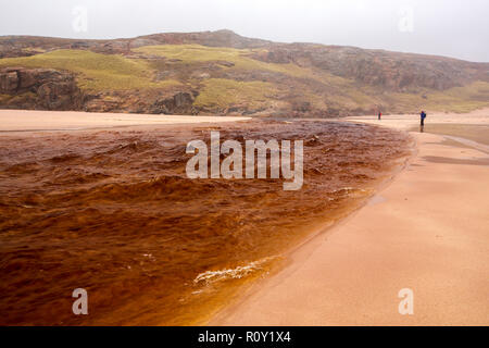 La sortie de Sandwood loch dans les conditions de crue traversant la plage de Sandwood Bay, Sutherland, Scotland, UK, avec l'eau tachée par la tourbe. Banque D'Images