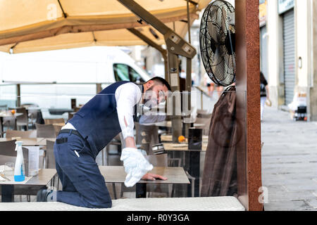 Florence, Italie - 31 août 2018 : waiter italien, l'homme en uniforme, chemise fenêtre de nettoyage avec un chiffon, solution de restaurant, café, à l'extérieur, outdo Banque D'Images