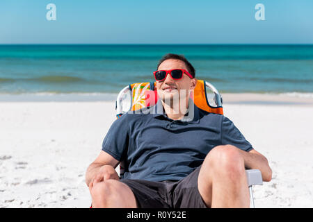 Happy man smiling face closeup lying on beach lounge chair au cours de journée ensoleillée avec des lunettes rouges en Floride avec l'eau de mer Banque D'Images