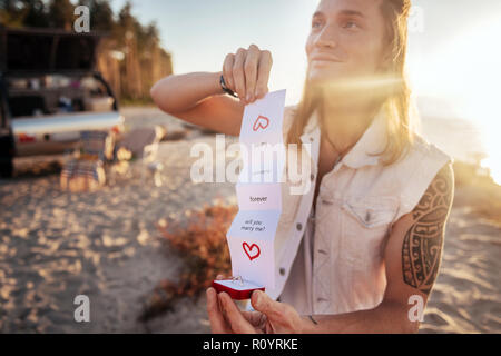 Transmission de blue-eyed man making sa femme proposition sur plage de sable Banque D'Images