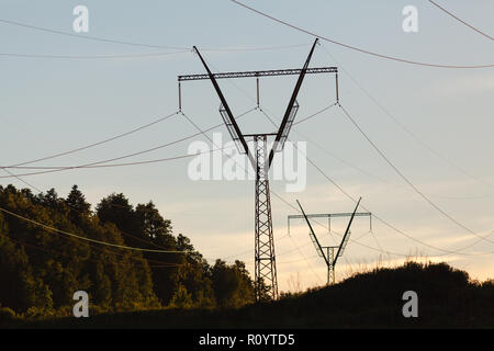 Pylônes électriques, les lignes électriques et les arbres silhouette sur un ciel nuageux au coucher du soleil Banque D'Images