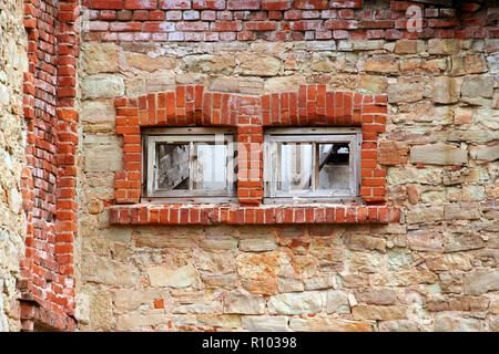 Deux fenêtres placardées dans un vieux bâtiment abandonné, les fenêtres sont bordées de brique rouge, un mur de brique jaune et rouge, un morceau de matériel Banque D'Images