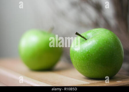 Pommes Granny Smith vert brillant sur bois naturel avec des branches en arrière-plan Banque D'Images