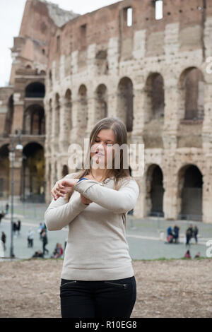 Smiling girl wearing white pull devant le Colisée, Rome, Italie, regarde sa montre Banque D'Images