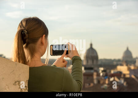 Jeune femme portant pull vert sur le toit en face de la cathédrale de Saint-Pierre, Vatican, Rome, Italie, prend des photos avec son smartphone Banque D'Images