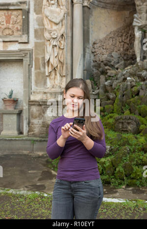 Jeune femme dans la Villa Aldobrandini, Frascati, Italie, en face de la fontaine antique, texting with smartphone Banque D'Images