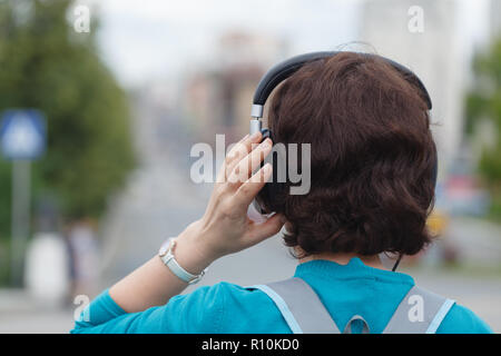 Girl revenir en arrière à l'écoute de la musique sous arbre en ville Banque D'Images