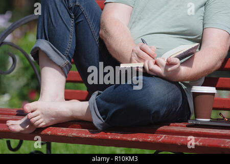 Homme assis sur le banc au parc écrit dans son carnet d'inspiration de travail Banque D'Images