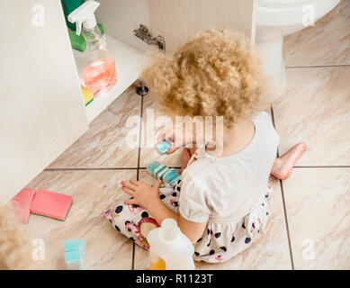 Petite fille sans surveillance jouer tranquillement à une salle de bains privative avec produits chimiques ménagers dangereux. Pour la sécurité à la maison concept. Garder hors de la portée des enfants. Banque D'Images