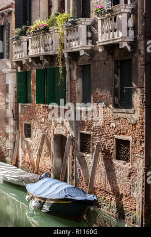 Les bâtiments en briques anciennes et peint avec des balcons et des portes avec couverts gondala bateaux sur les canaux de Venise Italie Banque D'Images