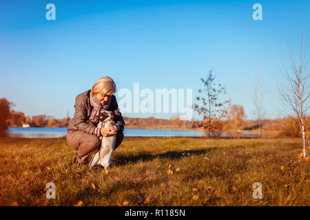 Balades maître chien pug in autumn park par rivière. Happy woman hugging pet. Banque D'Images