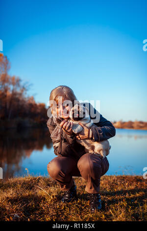 Balades maître chien pug in autumn park par rivière. Happy woman hugging pet. Banque D'Images