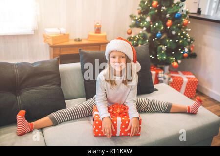 Petit et happy girl posing sur appareil photo. Elle a l'air heureux. Fille est assise sur la ficelle et s'appuie sur la case rouge avec l'heure actuelle. Elle a l'air sur l'appareil-photo. Jeune fille est la seule à ro Banque D'Images