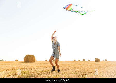 Portrait of happy woman smiling 20s et jouer avec flying kite au cours de promenade à travers champ d'or au cours de journée ensoleillée Banque D'Images