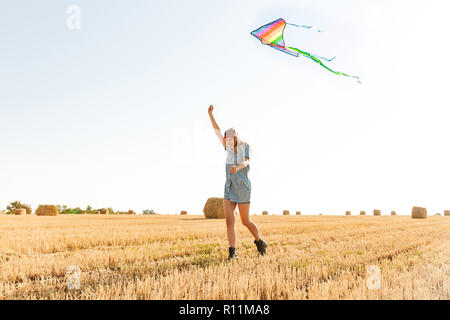 Portrait de femme élégante 20s de sourire et de jouer avec flying kite au cours de promenade à travers champ d'or au cours de journée ensoleillée Banque D'Images