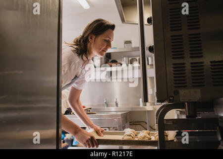 Female Baker de placer un bac de scones cuits au four. Banque D'Images