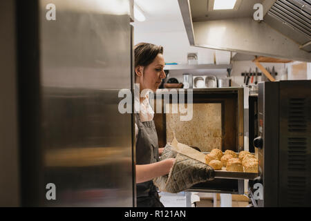 Female baker dépose un plateau de scones cuits hors du four. Banque D'Images