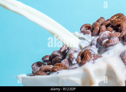 Flux de lait et verser dans une tasse avec copeaux de chocolat sous forme d'anneaux, des éclaboussures de lait sur un fond bleu clair Banque D'Images