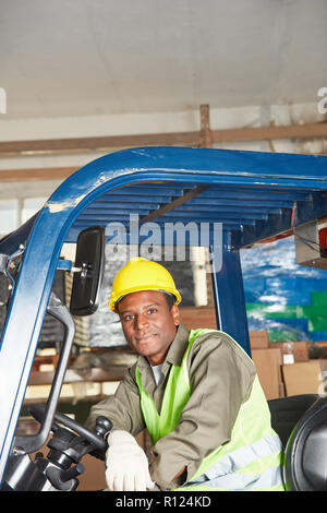 Homme africain sur le chariot élévateur fonctionne comme un pilote dans l'entrepôt Banque D'Images