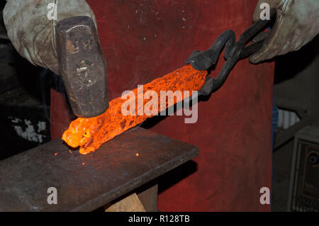 Red hot de la chaleur intense d'une forge, le forgeron travaille habilement le contour de métal en un couteau à la main. Banque D'Images