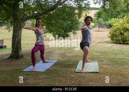 L'homme et de la femme faisant du yoga à jardin, pratiquer warrior pose Banque D'Images