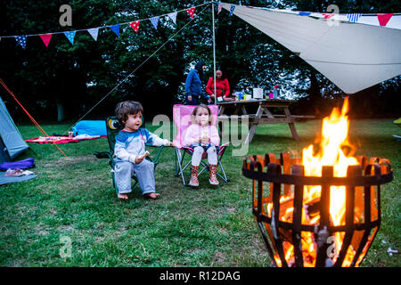 Les enfants se détendre en face de Bonfire, parents en arrière-plan Banque D'Images