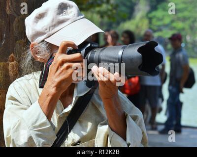 Photographe de rue vietnamiens âgés prend des photos spontanées avec son appareil photo reflex numérique Nikon avec un téléobjectif. Banque D'Images