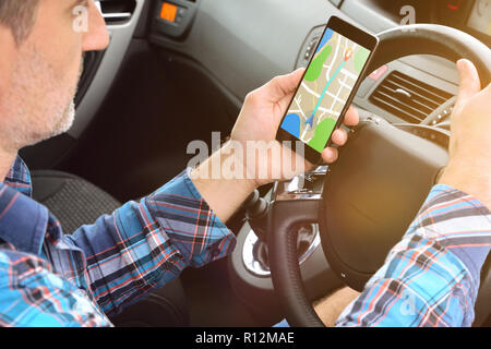 Man consulting un itinéraire sur un téléphone cellulaire avec une application pour atteindre sa destination dans une voiture. Vue arrière élevée Banque D'Images