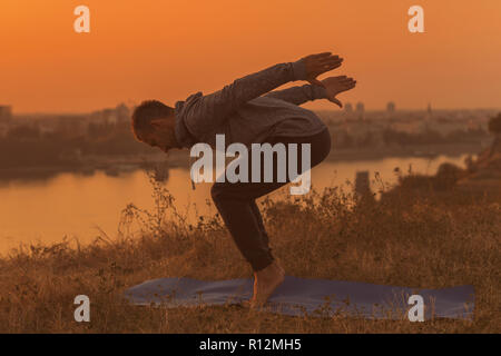 Man doing yoga sur le coucher du soleil avec vue sur la ville, Banque D'Images