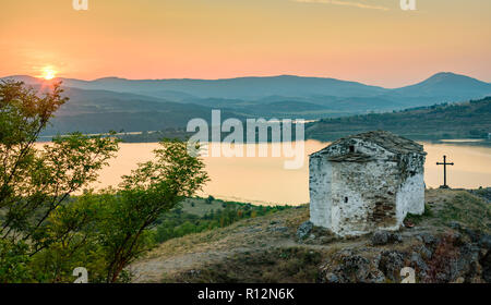 Petite chapelle en pierre sur une colline sous les derniers rayons du soleil couchant - belle image, représentant la puissance de la foi en la religion orthodoxe Banque D'Images